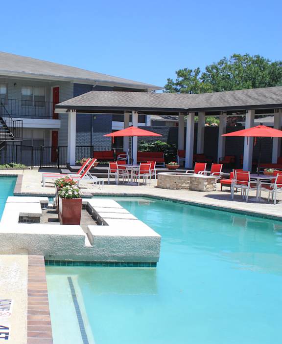 A pool with red chairs and a building in the background.