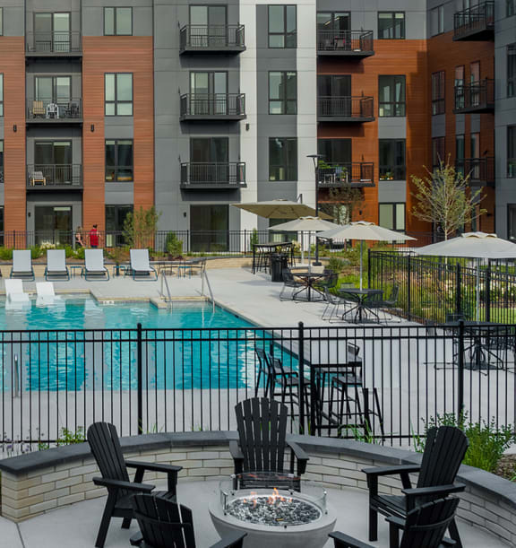 a swimming pool with chaise lounge chairs and tables in front of an apartment building