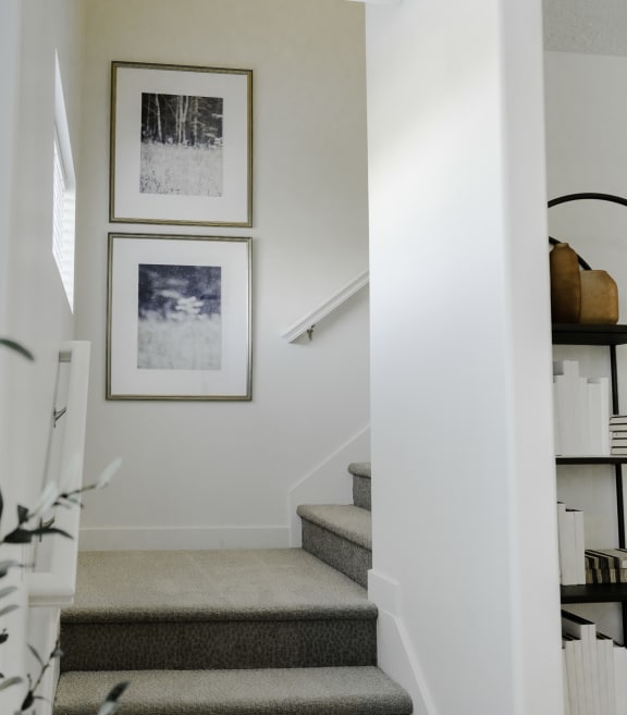 a view from the bottom of the stairs of a white staircase with two pictures on the wall