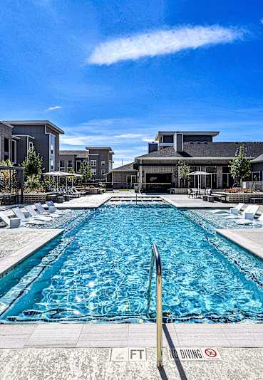 A large outdoor swimming pool surrounded by lounge chairs and buildings.