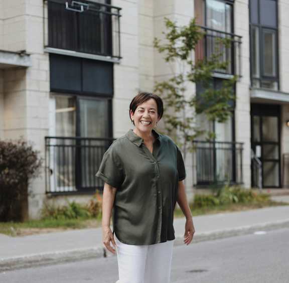 A woman in a green shirt and white pants stands on a street.