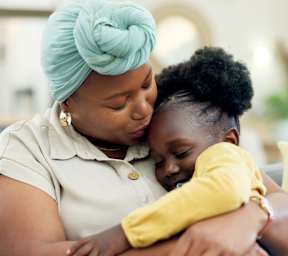 A woman in a turquoise head wrap is hugging a child.