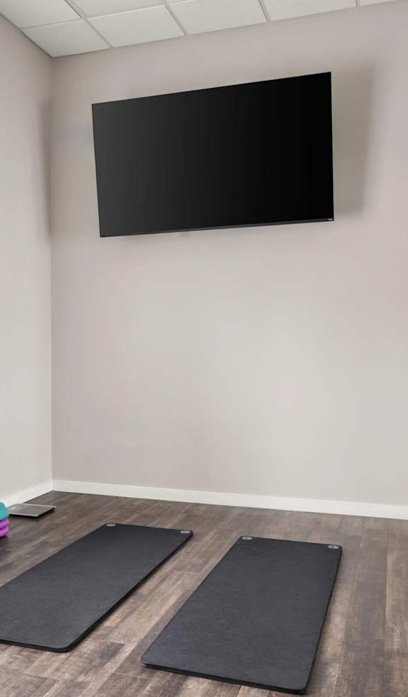 A room with a flat screen TV mounted on the wall, a couple of exercise balls, and yoga mats on the floor.