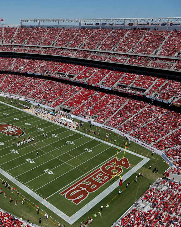 A stadium full of red seats with a football game taking place.