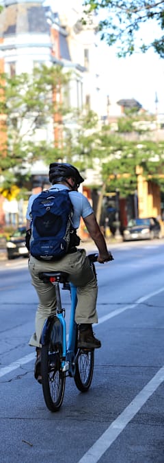 A man with a blue backpack is riding a blue bicycle on a city street.