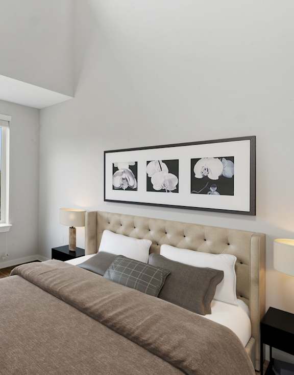 A bedroom with a large bed, a chair, a table, and a framed picture on the wall.