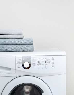 A white washing machine with a stack of towels on top.