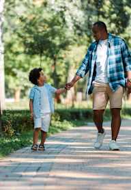 A man and a child are walking hand in hand on a path in a park.