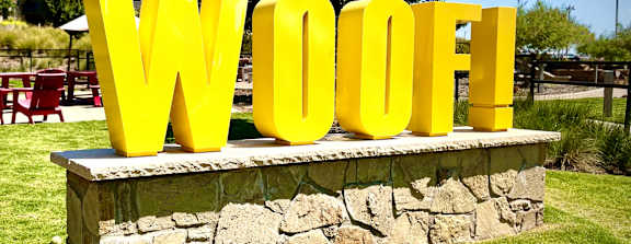 A large yellow Woof! sign sits on a stone platform in a grassy area.