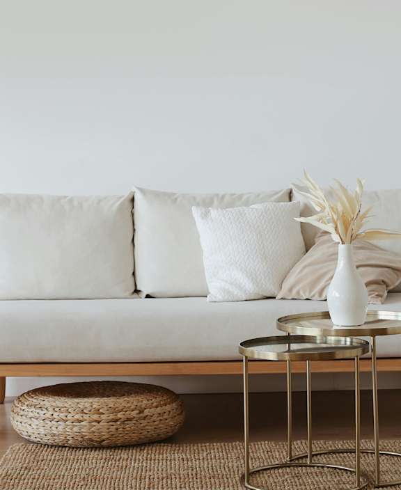 A white sofa with a woven basket and a glass table with a vase on it.
