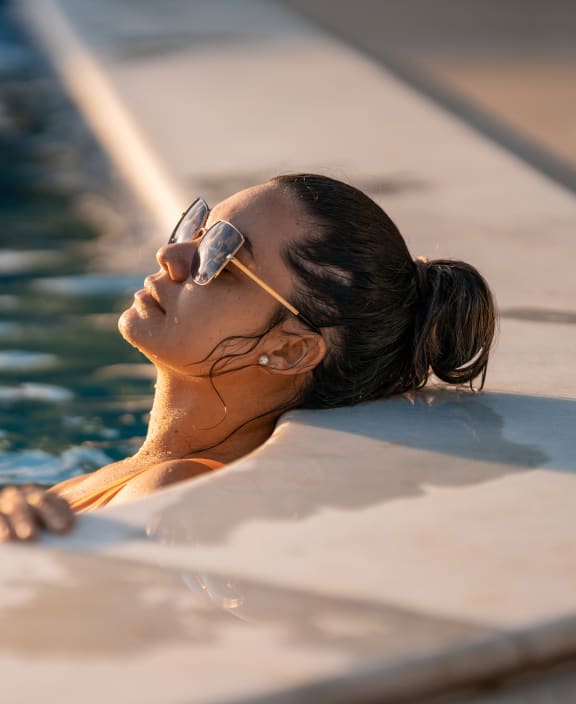 Woman in shades relaxing at the corner of a swimming pool.