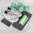 A pair of grey sneakers, a pair of green dumbbells, a black smartphone, and a green yoga mat are arranged on a grey surface.