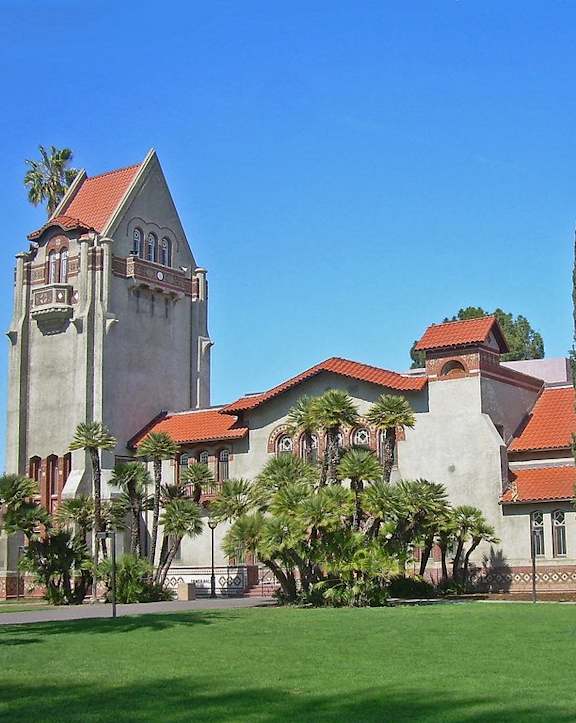 A large building with a tower and a red roof is surrounded by trees.