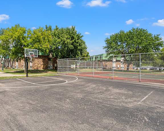 a basketball court in a park with trees and a building in the background