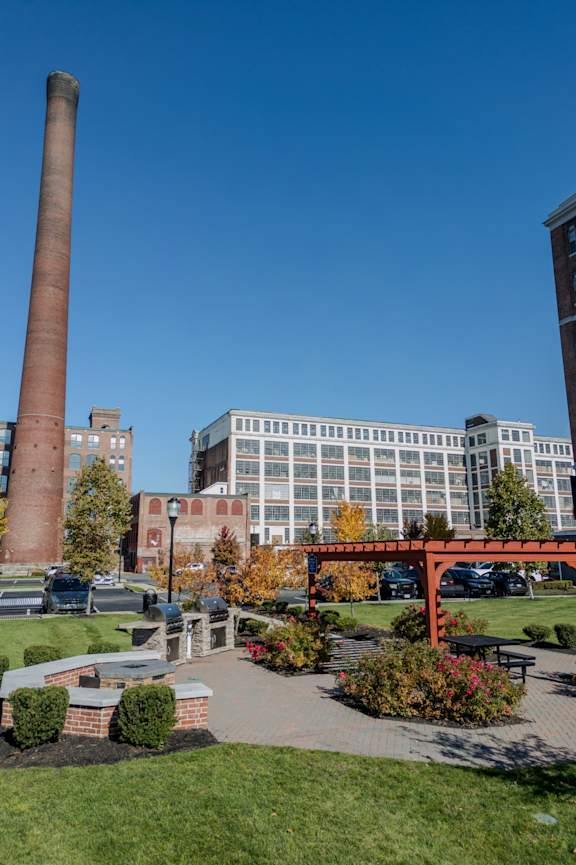 A tall brick chimney stands next to a large building with a parking lot in front.