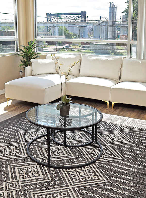 A living room with a white couch, a glass coffee table, and a black and white rug.