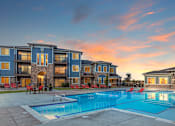 Thumbnail 16 of 32 - A swimming pool in front of a building with a sunset in the background.