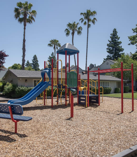 a playground with a slide and benches in front of a house at Woodbridge Apartments, CA 95833