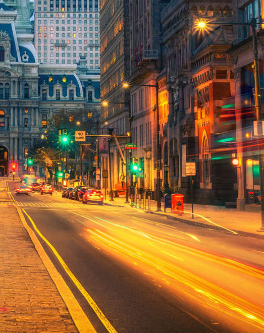 A long exposure shot of a city street at night with light trails from moving vehicles.