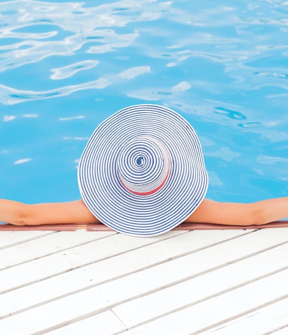 A woman in a striped hat is relaxing by the pool.