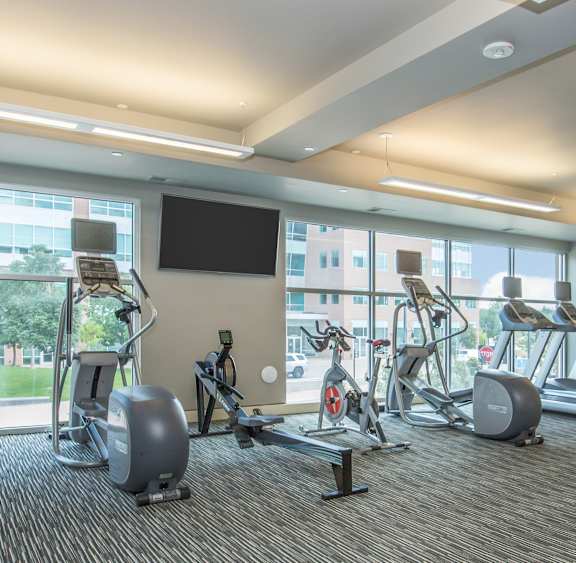 a gym with weights and cardio equipment on the floor and large windows