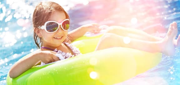 Little Girl in Sunglasses Laying in Inner Tube in Pool and Smiling